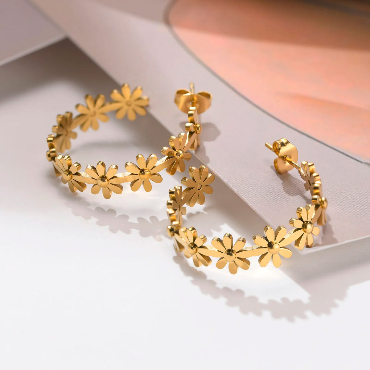 Gold-tone daisy floral hoop earrings with layered flower details and hinged stud backs