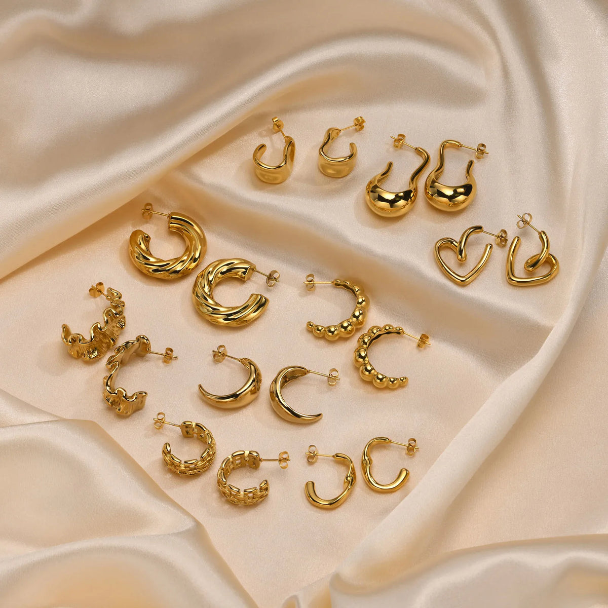 Gold-plated hoop earrings laid out, including heart and swirl designs
