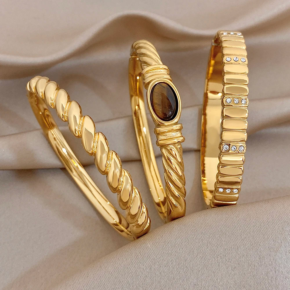 Gold-tone twisted cuff bangles with dark oval stone and rhinestone accents