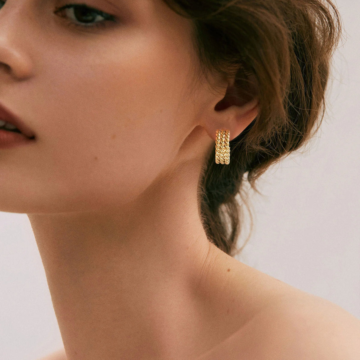 Gold-tone rope-twist hoop earring worn on the earlobe, shown from the side