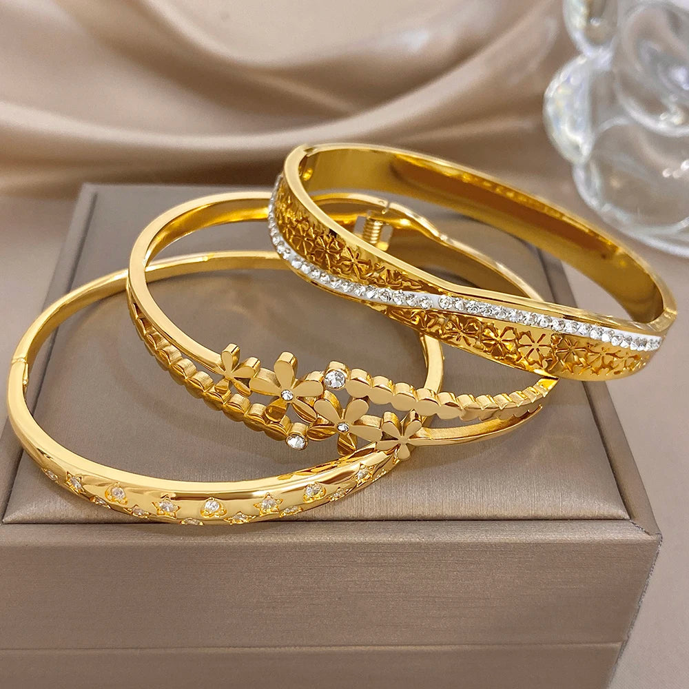 Stackable gold cuff bangles with etched patterns, daisy charms, and clear stones