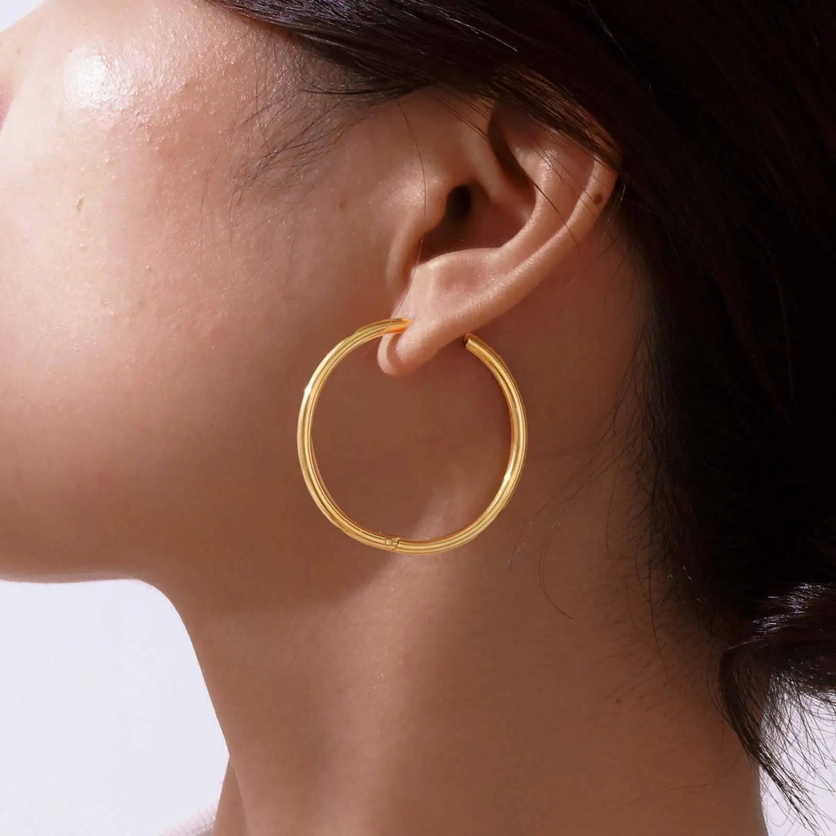 Large gold hoop earring worn on an ear.