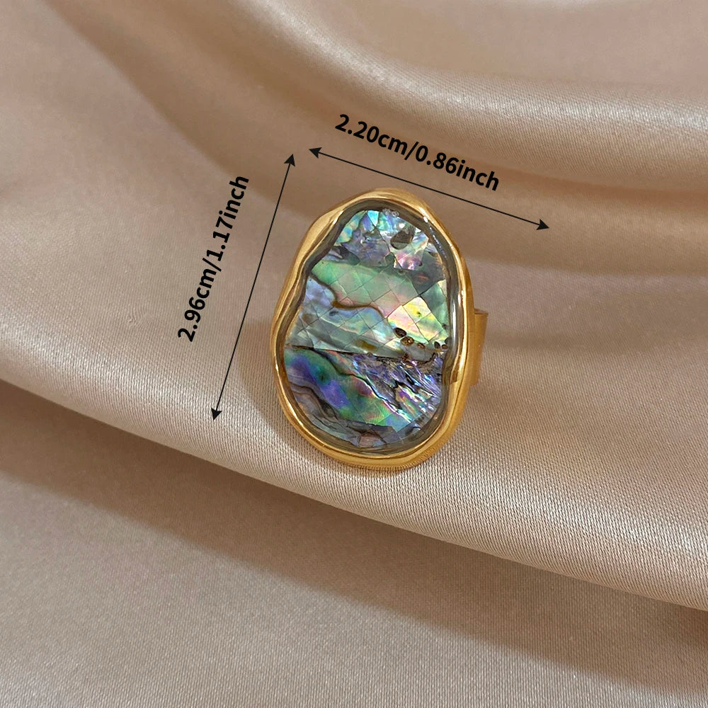 Gold-plated abalone shell chunky ring close-up on neutral fabric, oval iridescent stone
