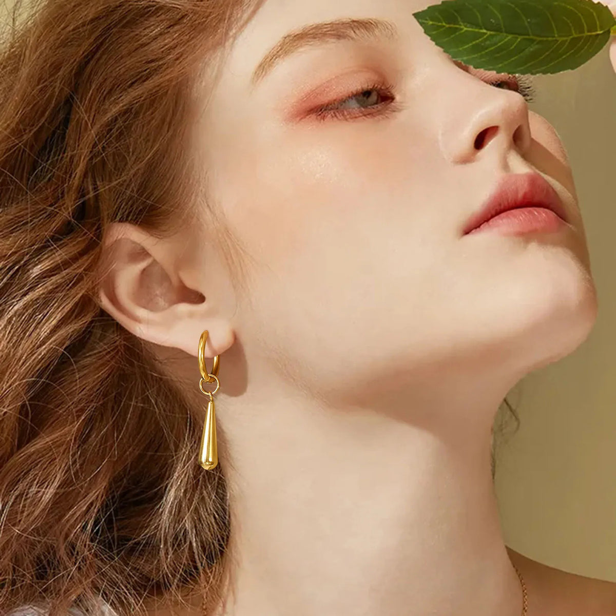 Gold-tone drop hoop earring with a tapered pendant, worn on the ear
