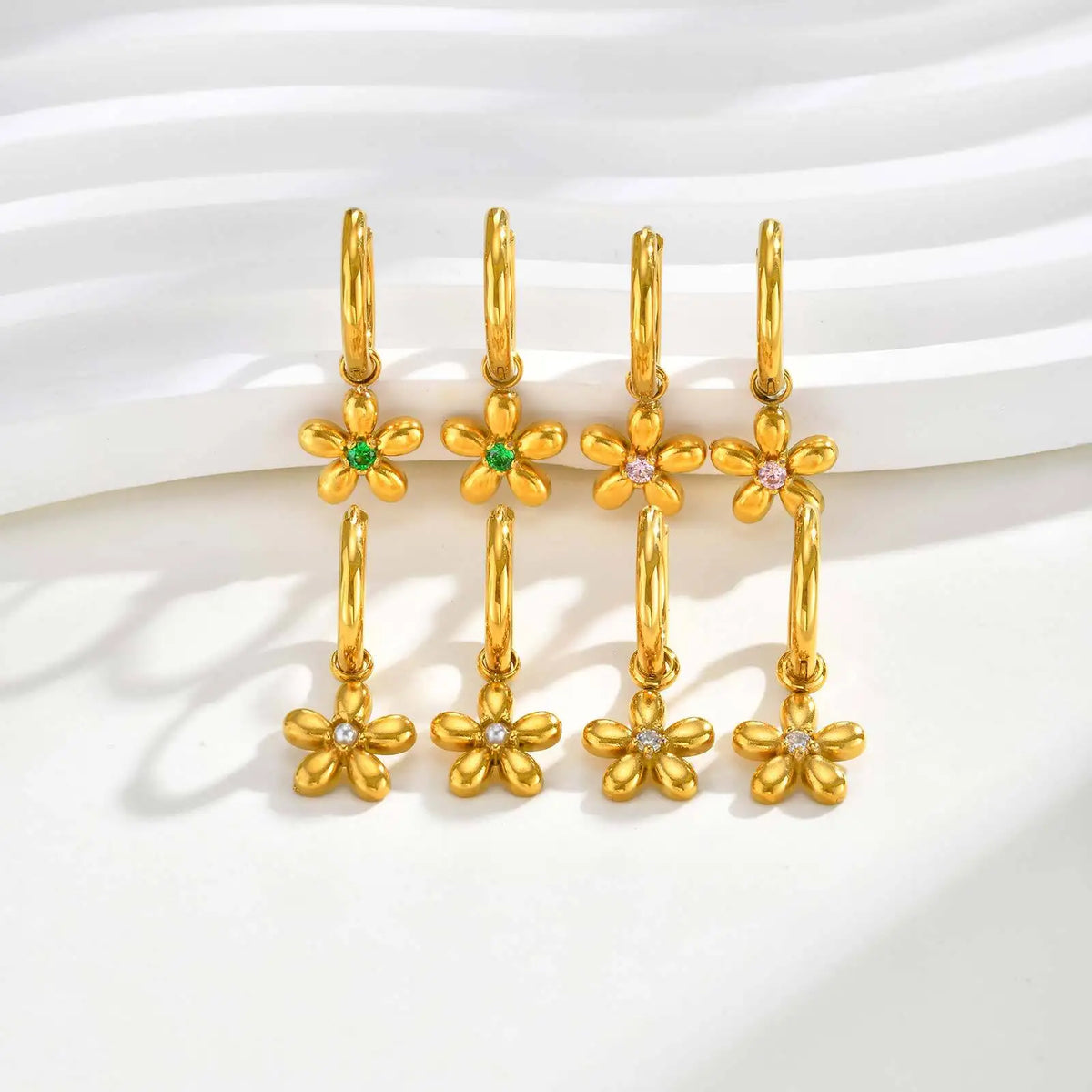 Gold flower charm hoop earrings shown in rows with clear, green, and pink center stones.