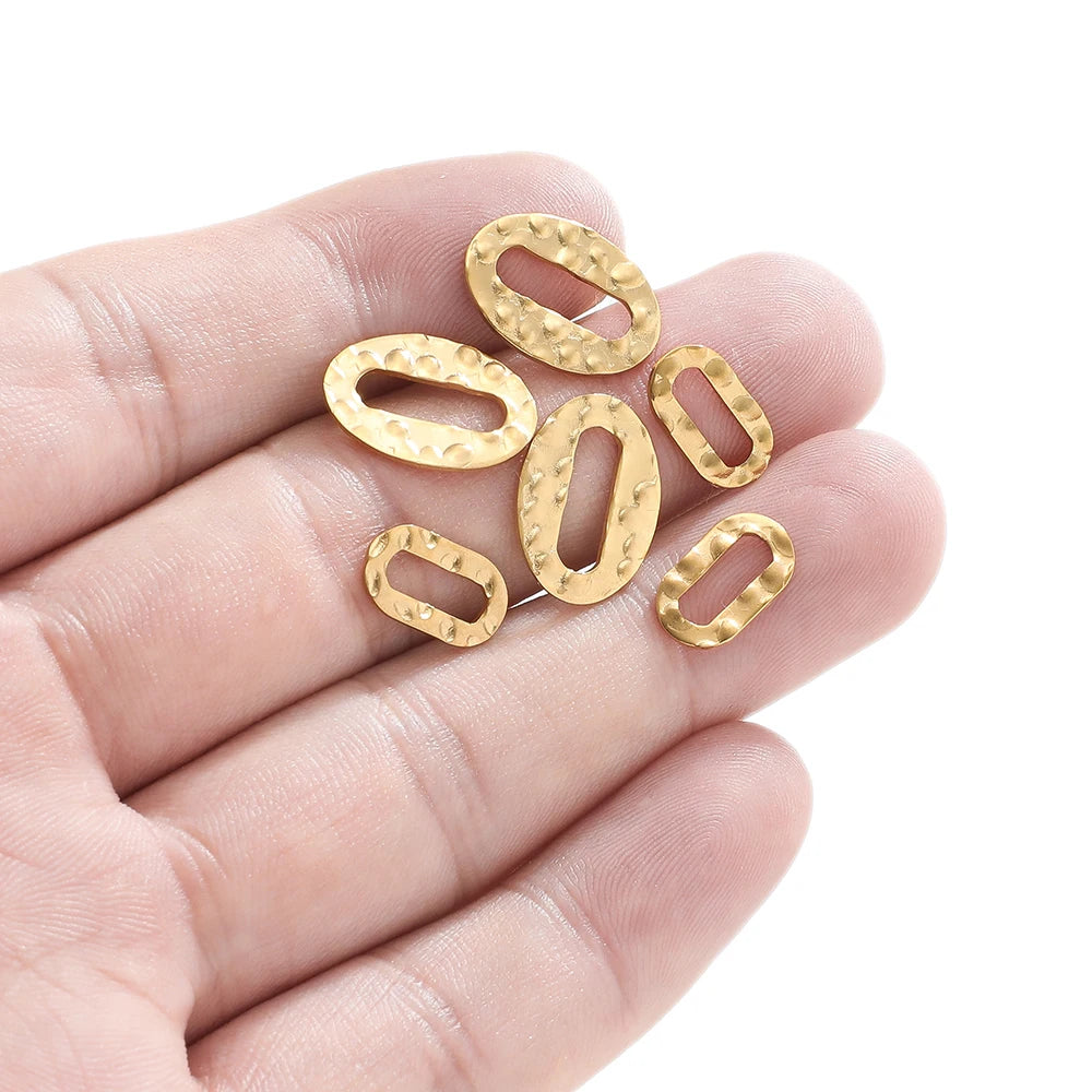 Gold hollow oval charm connectors held in hand, hammered texture, small oval openings