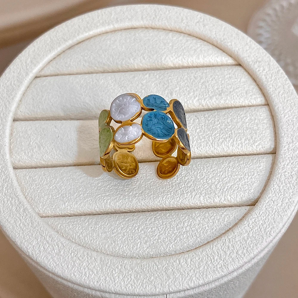 Gold-tone open cuff bracelet with blue and white enamel leaf coin accents and green leaves